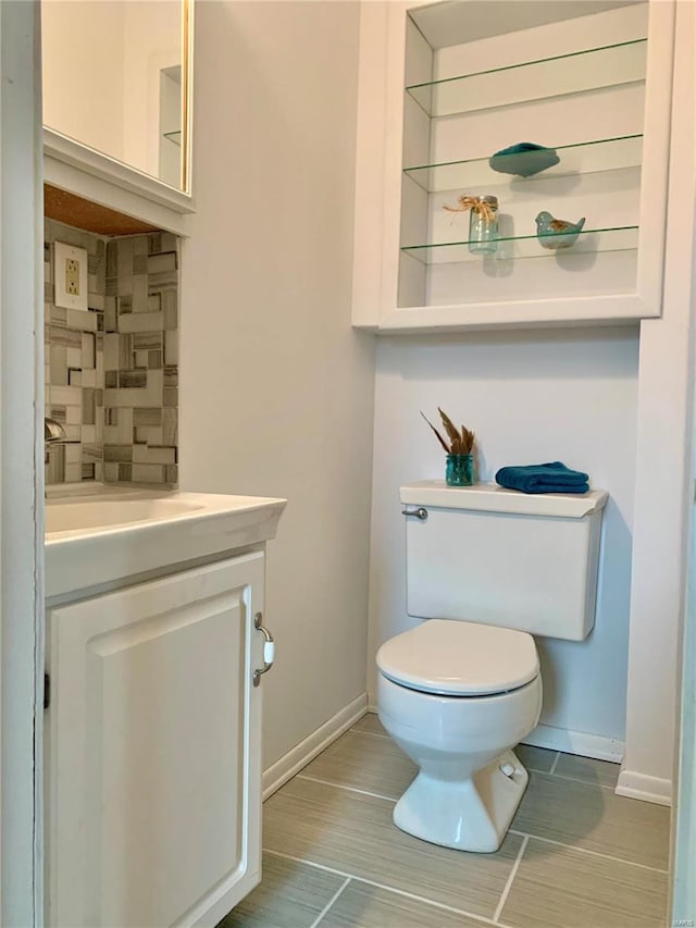 half bath with vanity, toilet, baseboards, and backsplash