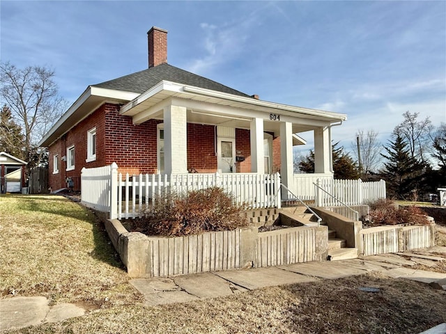 view of front of property with covered porch, brick siding, a chimney, and roof with shingles