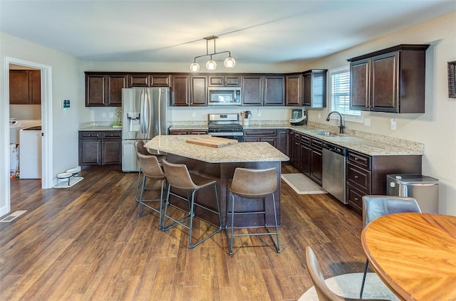 kitchen featuring a center island, sink, hanging light fixtures, stainless steel appliances, and washer / clothes dryer