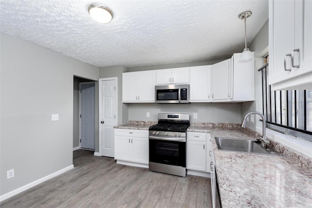 kitchen with light wood-type flooring, stainless steel appliances, sink, decorative light fixtures, and white cabinets