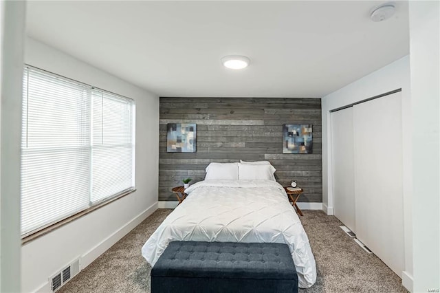 carpeted bedroom featuring wooden walls and a closet