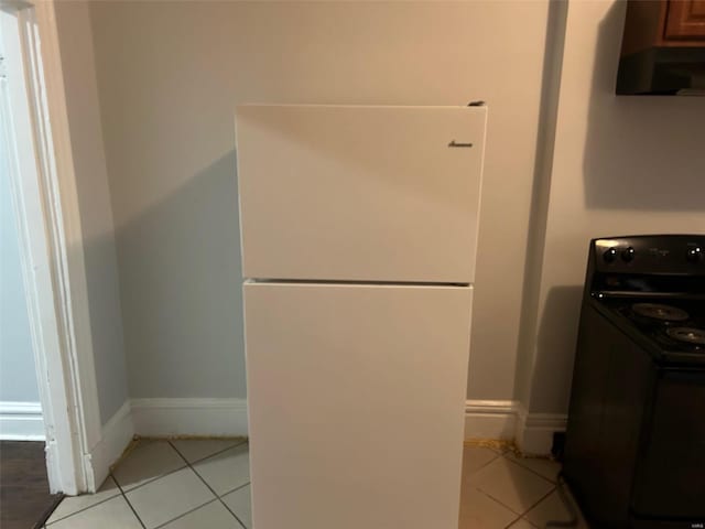 kitchen with ventilation hood, white fridge, light tile patterned flooring, and black range with electric stovetop