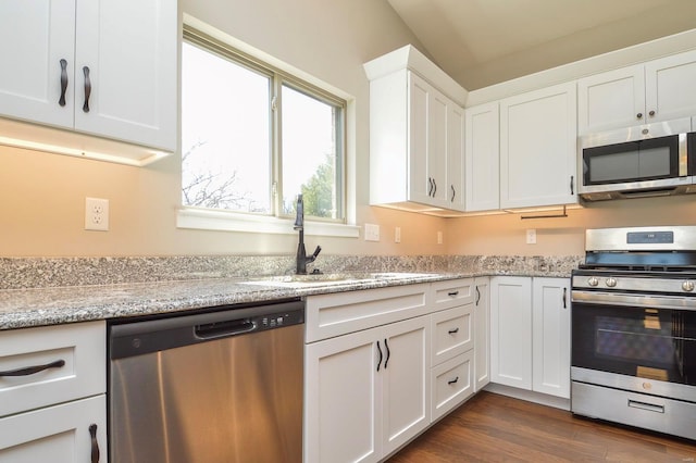 kitchen featuring a sink, light stone counters, appliances with stainless steel finishes, white cabinetry, and dark wood-style flooring