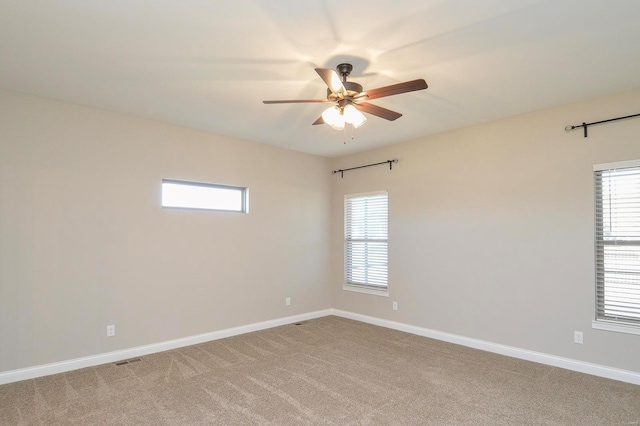 empty room featuring light colored carpet, visible vents, baseboards, and ceiling fan