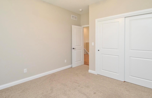 unfurnished bedroom with baseboards, visible vents, a closet, and light carpet