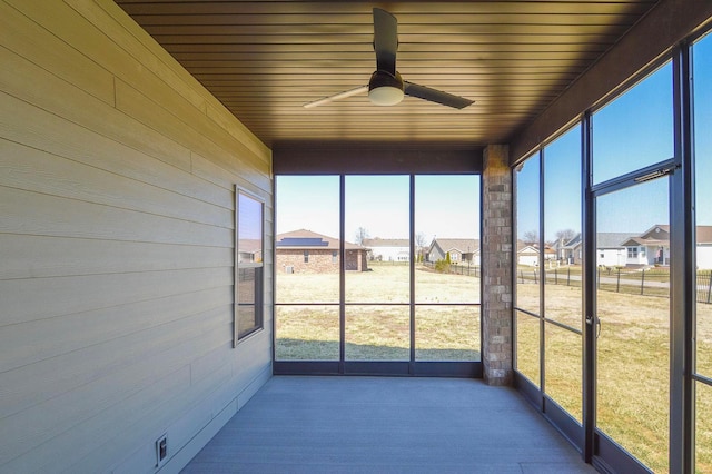 unfurnished sunroom featuring wood ceiling, a ceiling fan, and a residential view