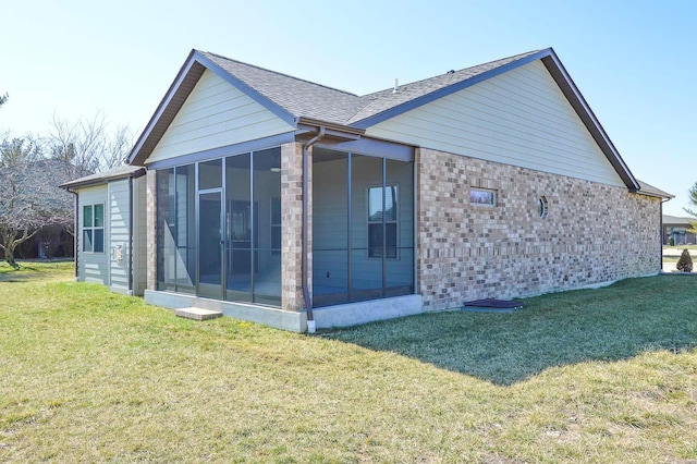 back of property with brick siding, a shingled roof, a yard, and a sunroom