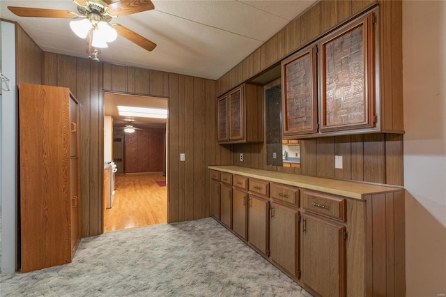 kitchen featuring ceiling fan, wood walls, and light carpet