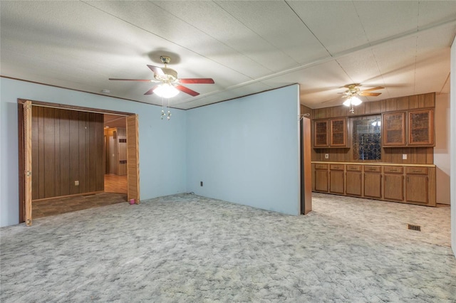 unfurnished living room with light carpet, a textured ceiling, ceiling fan, and wooden walls