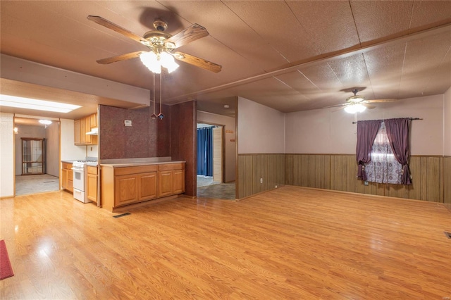 kitchen with ceiling fan, light hardwood / wood-style floors, a textured ceiling, wooden walls, and white gas range oven