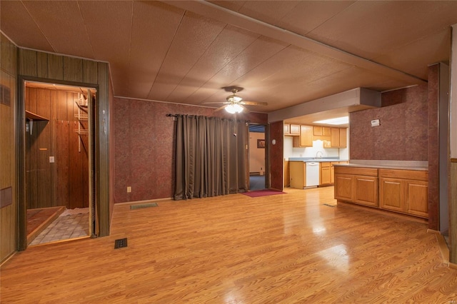 unfurnished living room with sink, light hardwood / wood-style floors, ceiling fan, and wood walls