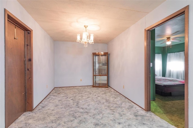 carpeted spare room featuring ceiling fan with notable chandelier