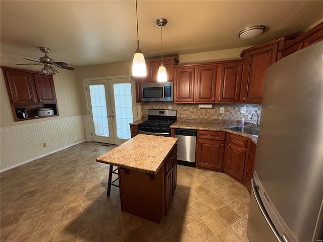 kitchen with french doors, sink, appliances with stainless steel finishes, decorative light fixtures, and a kitchen island