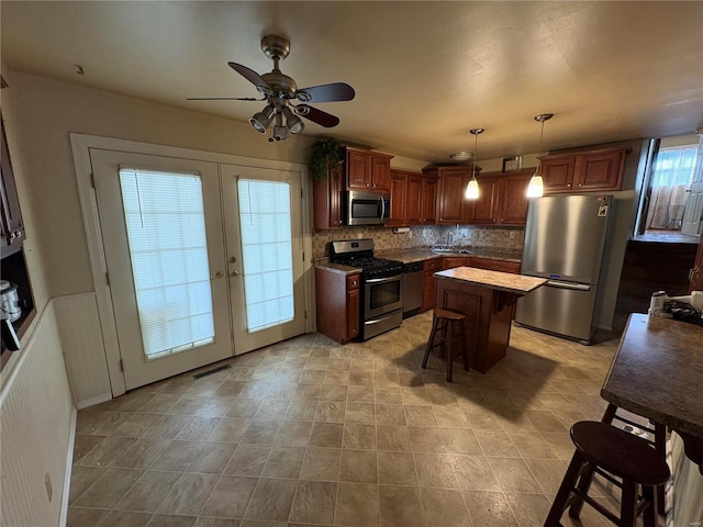 kitchen with french doors, a center island, a kitchen breakfast bar, decorative light fixtures, and appliances with stainless steel finishes