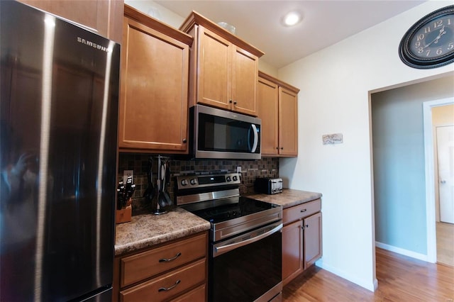 kitchen with backsplash, dark stone counters, stainless steel appliances, and light wood-type flooring