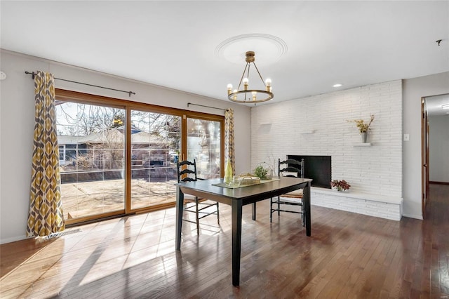 dining space featuring an inviting chandelier, a brick fireplace, and dark hardwood / wood-style flooring