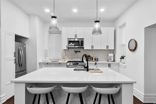 kitchen featuring sink, decorative light fixtures, stainless steel appliances, and an island with sink