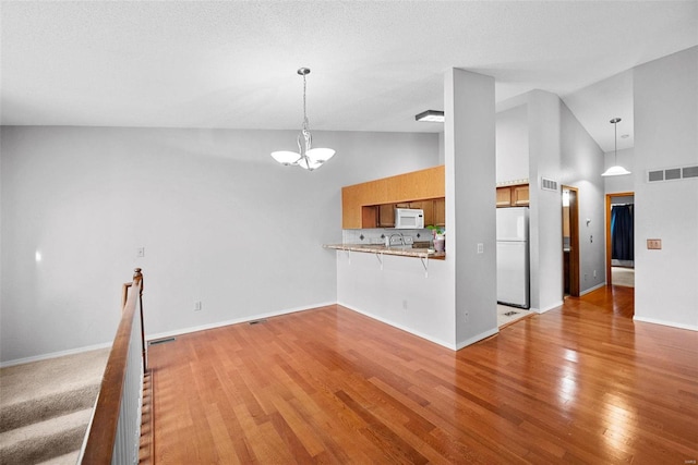 unfurnished living room featuring light wood-type flooring, high vaulted ceiling, an inviting chandelier, and sink