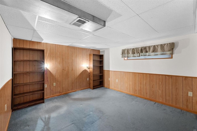 spare room featuring light colored carpet, a drop ceiling, and wood walls