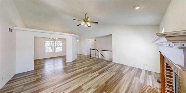 unfurnished living room featuring high vaulted ceiling, ceiling fan with notable chandelier, a fireplace, and light hardwood / wood-style flooring