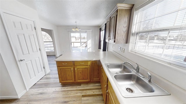 kitchen with pendant lighting, sink, a notable chandelier, a textured ceiling, and light hardwood / wood-style flooring