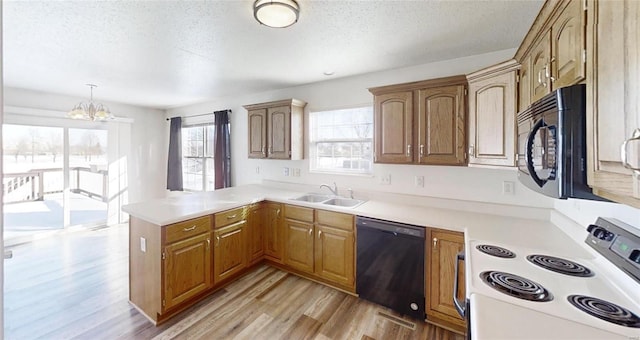 kitchen with sink, an inviting chandelier, black appliances, decorative light fixtures, and kitchen peninsula