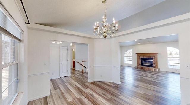 unfurnished dining area featuring a chandelier, a brick fireplace, and light wood-type flooring