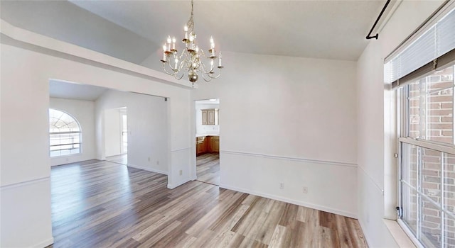 unfurnished dining area featuring lofted ceiling, a notable chandelier, and light wood-type flooring