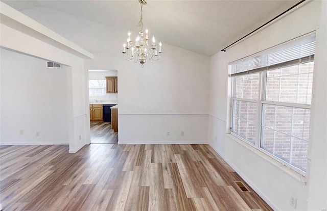 unfurnished dining area featuring lofted ceiling, light hardwood / wood-style floors, and a notable chandelier