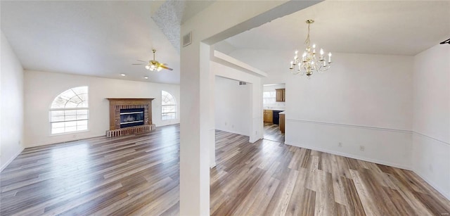 unfurnished living room featuring lofted ceiling, a brick fireplace, ceiling fan with notable chandelier, and wood-type flooring