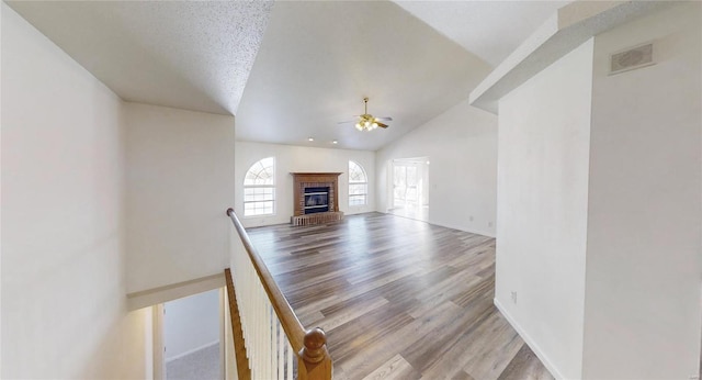 unfurnished living room featuring ceiling fan, high vaulted ceiling, light hardwood / wood-style floors, a textured ceiling, and a brick fireplace