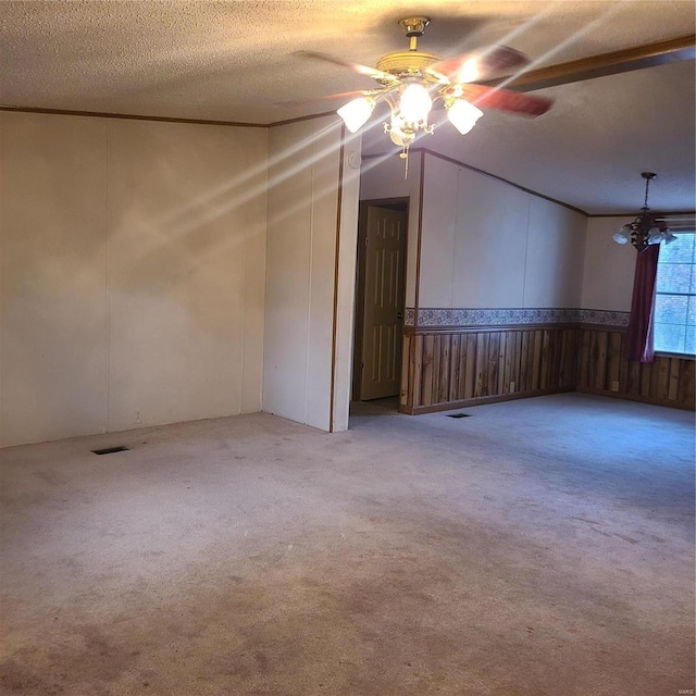 carpeted spare room featuring wooden walls, ceiling fan with notable chandelier, and a textured ceiling