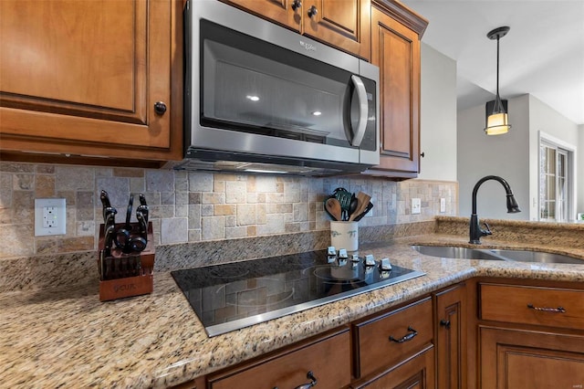 kitchen featuring light stone countertops, sink, hanging light fixtures, black electric cooktop, and decorative backsplash