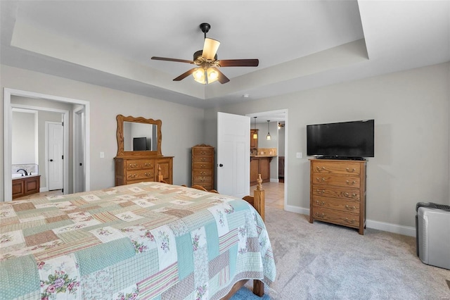 carpeted bedroom with a tray ceiling, ensuite bath, and ceiling fan