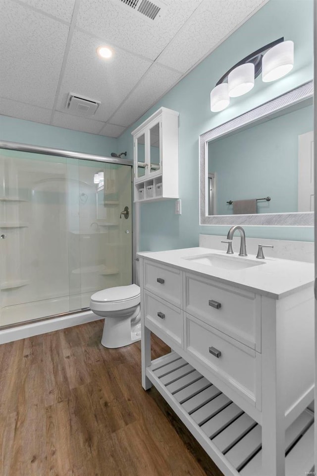 bathroom with wood-type flooring, toilet, a paneled ceiling, vanity, and a shower with shower door