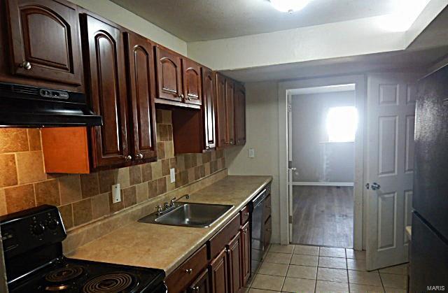 kitchen featuring tasteful backsplash, exhaust hood, sink, black appliances, and light tile patterned flooring