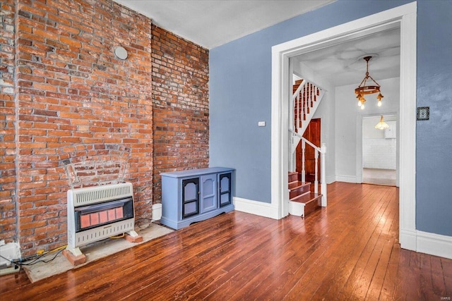 unfurnished living room with an inviting chandelier, heating unit, brick wall, and wood-type flooring