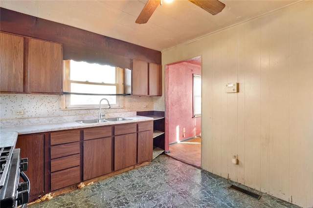 kitchen with sink, wood walls, ceiling fan, gas range oven, and backsplash