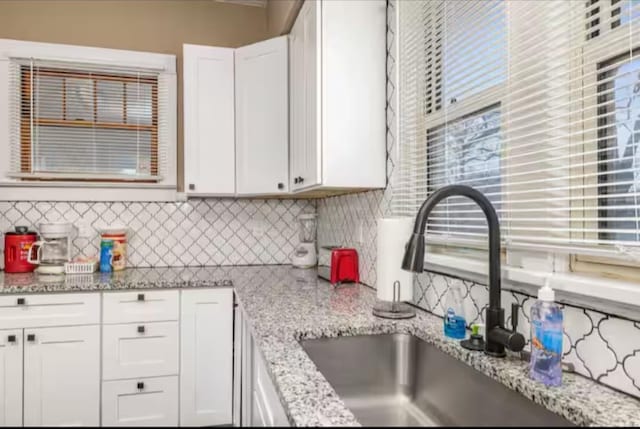 kitchen with backsplash, light stone counters, white cabinetry, and sink