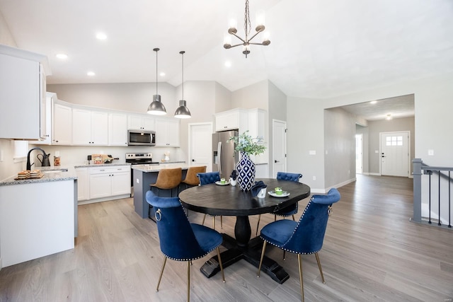 dining area with light hardwood / wood-style flooring, a chandelier, vaulted ceiling, and sink