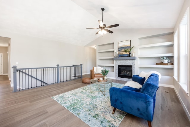 living room featuring built in shelves, a healthy amount of sunlight, vaulted ceiling, and hardwood / wood-style flooring