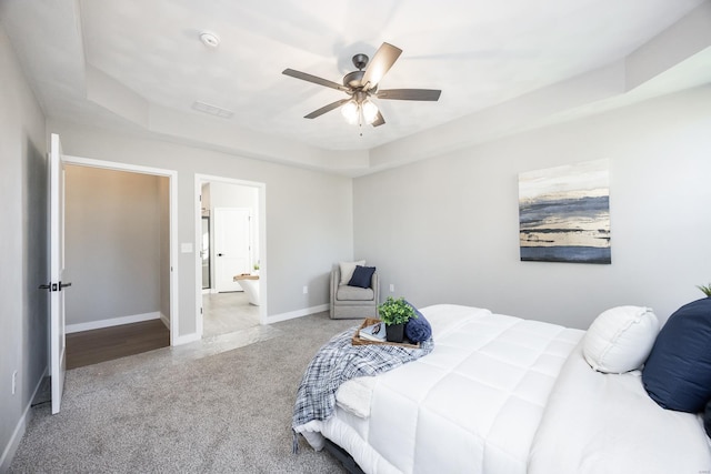 carpeted bedroom featuring ceiling fan, a raised ceiling, and connected bathroom