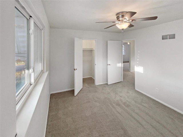 unfurnished bedroom with a walk in closet, ceiling fan, and light colored carpet