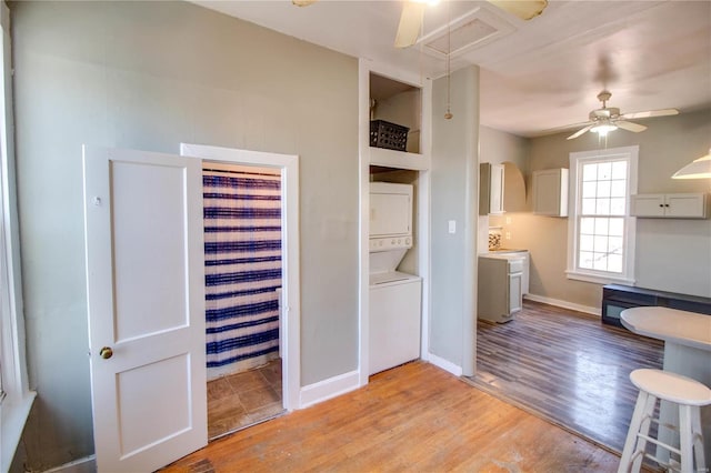 kitchen with baseboards, a ceiling fan, stacked washer / dryer, light wood-style flooring, and light countertops