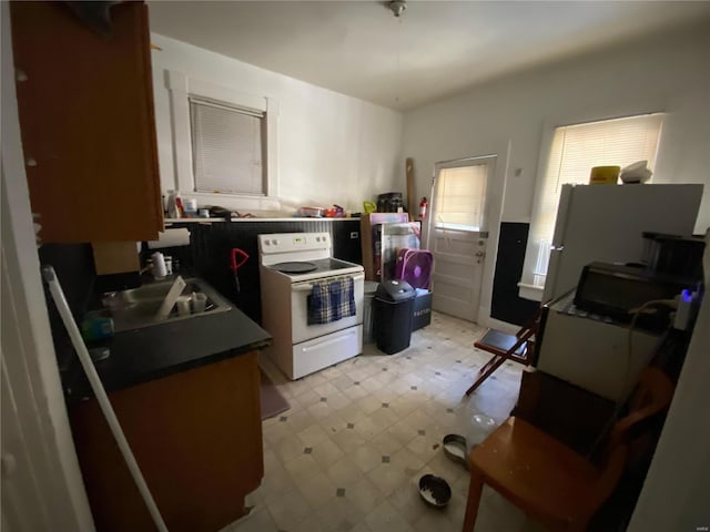 kitchen with white electric stove, brown cabinetry, dark countertops, light floors, and a sink