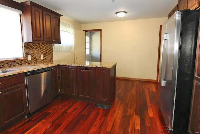 kitchen with kitchen peninsula, decorative backsplash, light stone counters, stainless steel appliances, and dark wood-type flooring