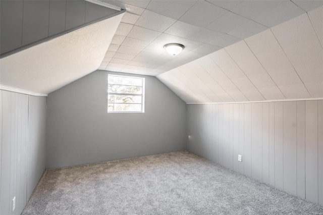 bonus room featuring carpet floors, vaulted ceiling, and wood walls