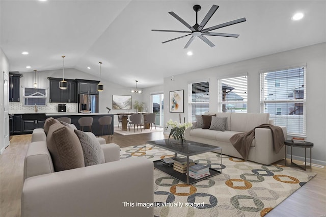 living room with plenty of natural light, ceiling fan with notable chandelier, light hardwood / wood-style floors, and lofted ceiling