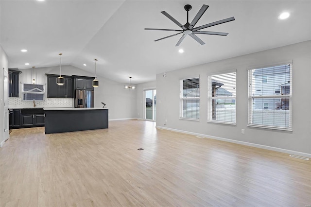 unfurnished living room featuring ceiling fan with notable chandelier, light wood-type flooring, vaulted ceiling, and plenty of natural light