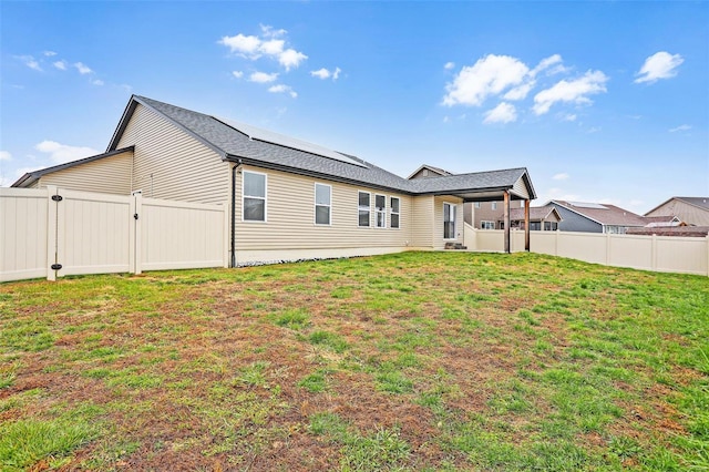 rear view of property with a lawn and solar panels